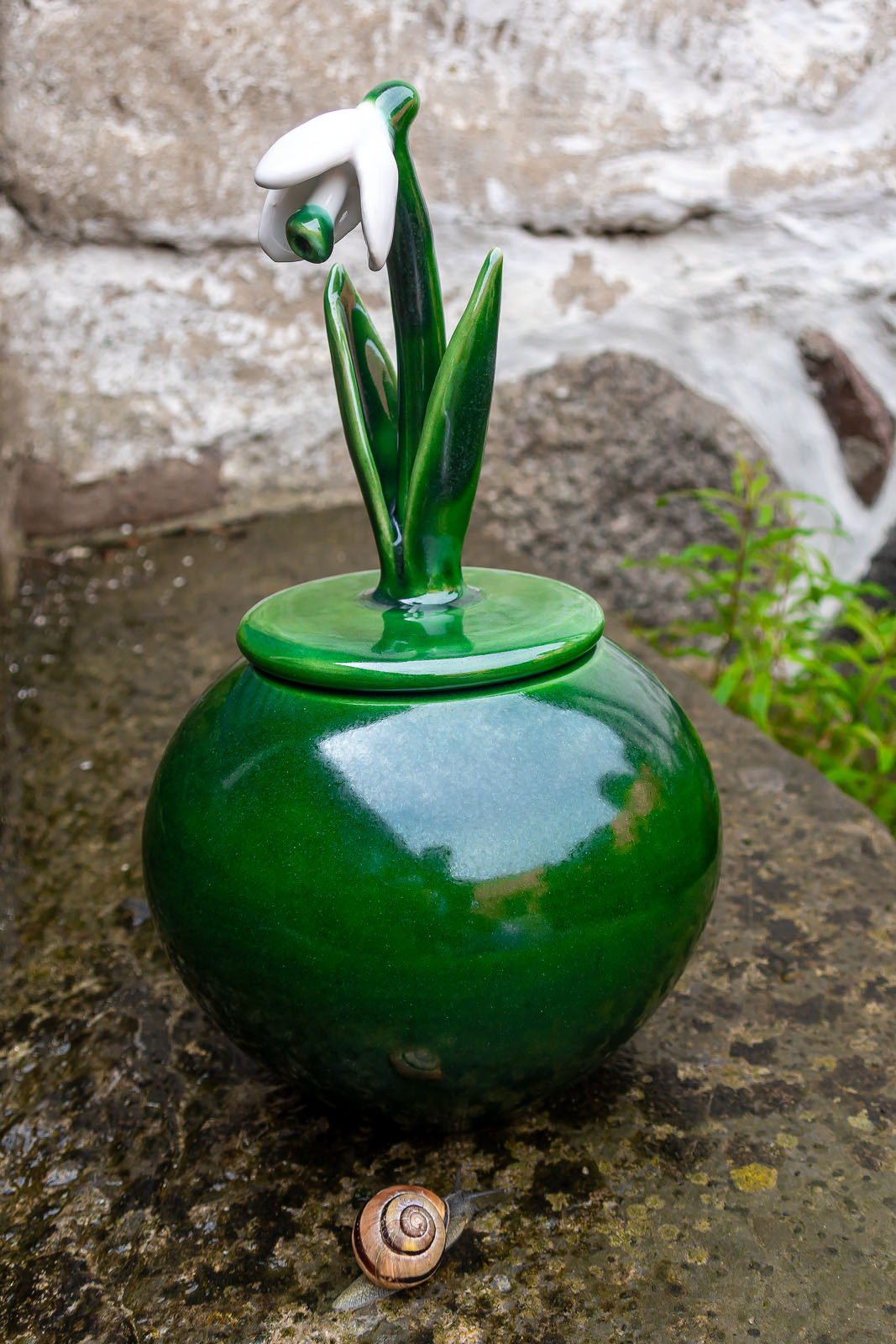 Burk med snödroppe på trappen.Snigel närmar sig. Keramik Elna-Karin.